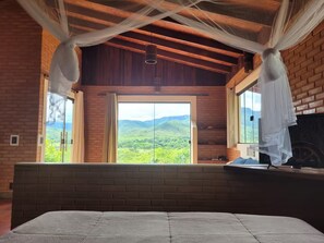 Une chambre avec un grand lit, une vue sur des collines verdoyantes et un plafond en bois.