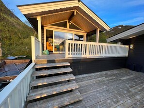 A wooden deck with steps leading to a covered patio area, a small outdoor seating area, and a view of a mountainous landscape.