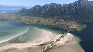 An aerial view of a coastal area with mountains, a sandy beach, and a road leading to the beach.