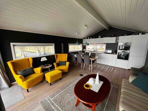 Un intérieur moderne comprenant un coin repas, des fauteuils jaunes, une table ronde et une cuisine avec des meubles blancs et des appareils en acier inoxydable.