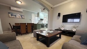 Una sala de estar con sofá, una mesa de centro, televisor y cocina al fondo.