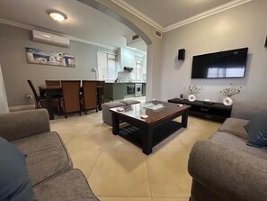 A living room with a sofa, a coffee table, a TV, and a kitchen in the background. - Beachfront Luxury 7 Chaka's Place Ballito (Ballito)