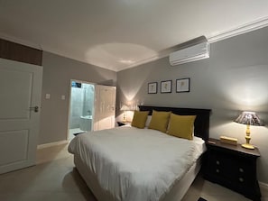 A bedroom with a bed, bedside lamps, a nightstand, and a door leading to a bathroom. - Beachfront Luxury 7 Chaka's Place Ballito (Ballito)