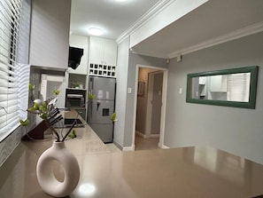 A modern kitchen with white cabinets, a refrigerator, and a vase with branches. - Beachfront Luxury 7 Chaka's Place Ballito (Ballito)