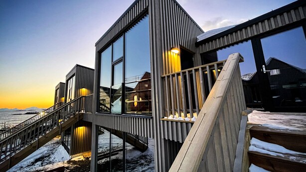 A modern building with a glass facade, a wooden staircase, and a view of the water.