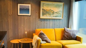 A modern living room with a wooden ceiling, a yellow sofa, a small round table, and two framed pictures on the wall.