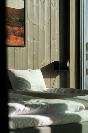 A bed with white bedding, a mounted picture frame, and a wall-mounted light fixture.