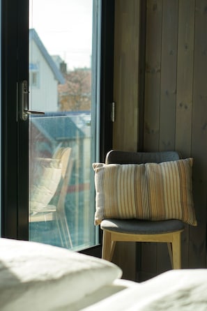 Una habitación con una cama, una silla con un cojín a rayas y vistas a través de un ventanal.