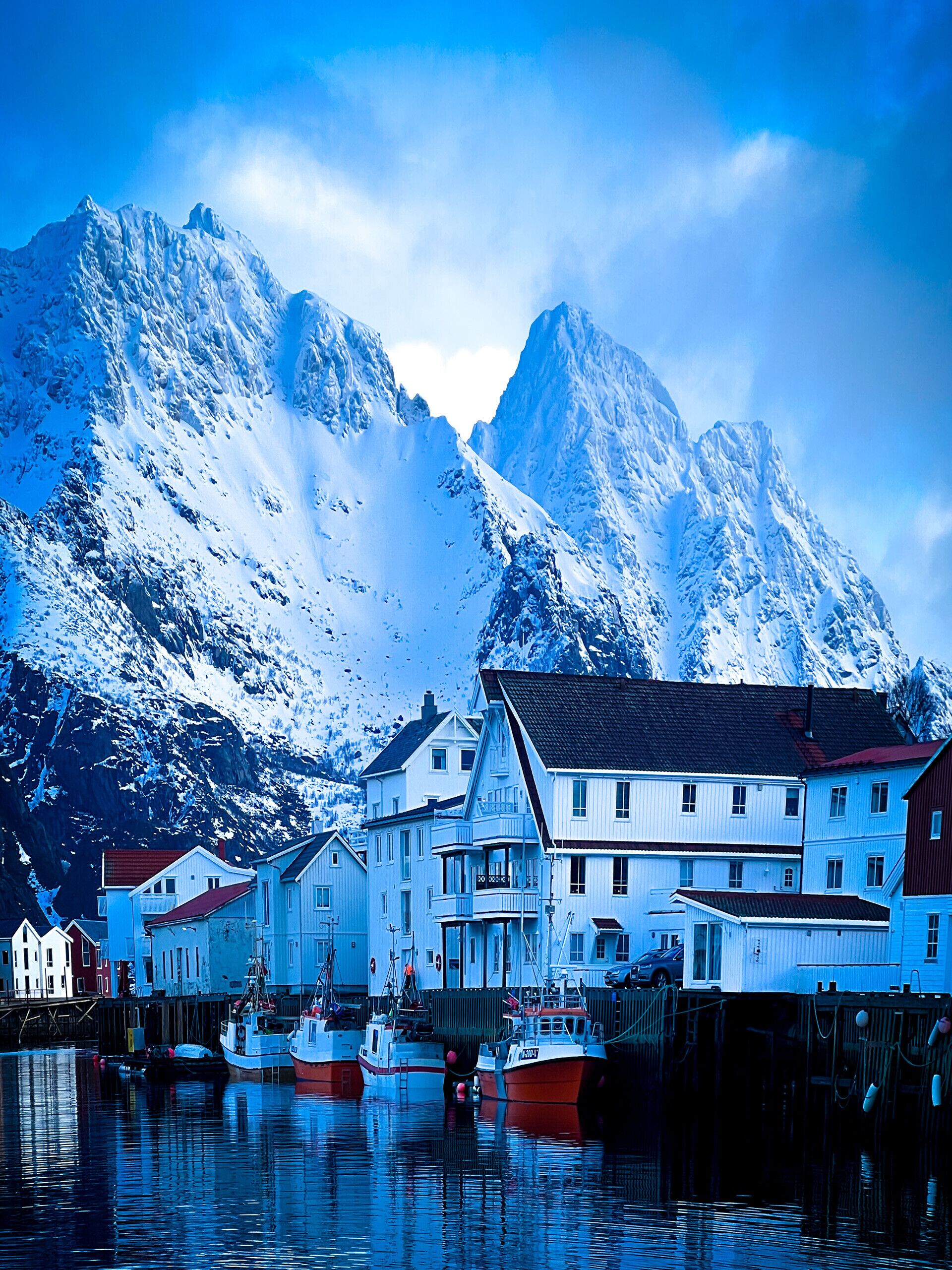 Eine Stadt am Wasser mit Gebäuden, Booten und verschneiten Bergen im Hintergrund.