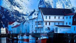 A waterfront town with buildings, boats, and snow-covered mountains in the background.