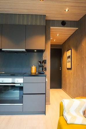 Una cocina moderna con armarios grises, una estufa y una cafetera. Hay una silla amarilla con una manta.
