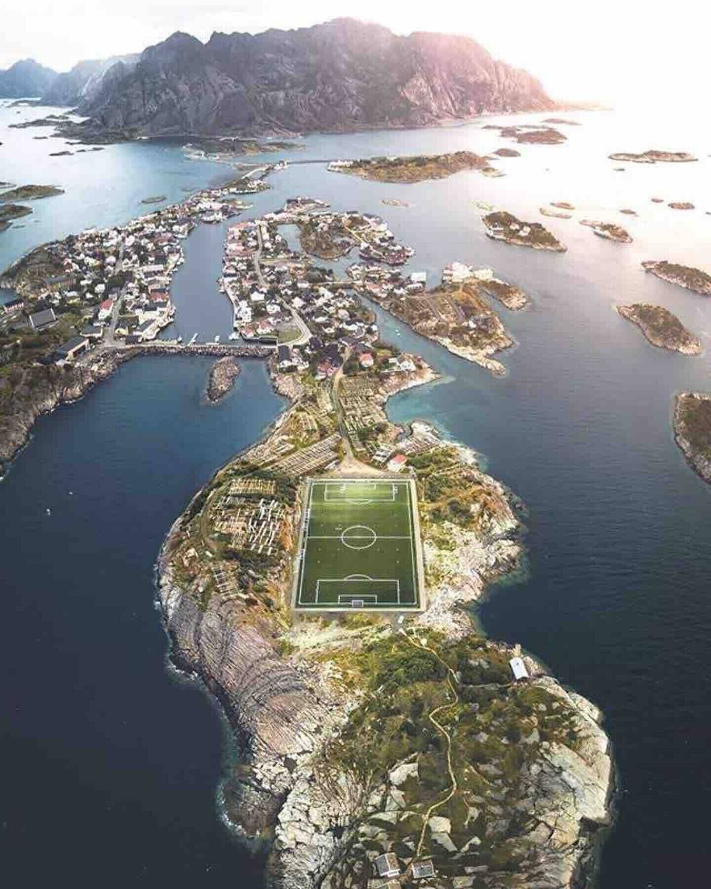 An aerial view of a coastal area with a prominent soccer field surrounded by residential buildings and small islands.