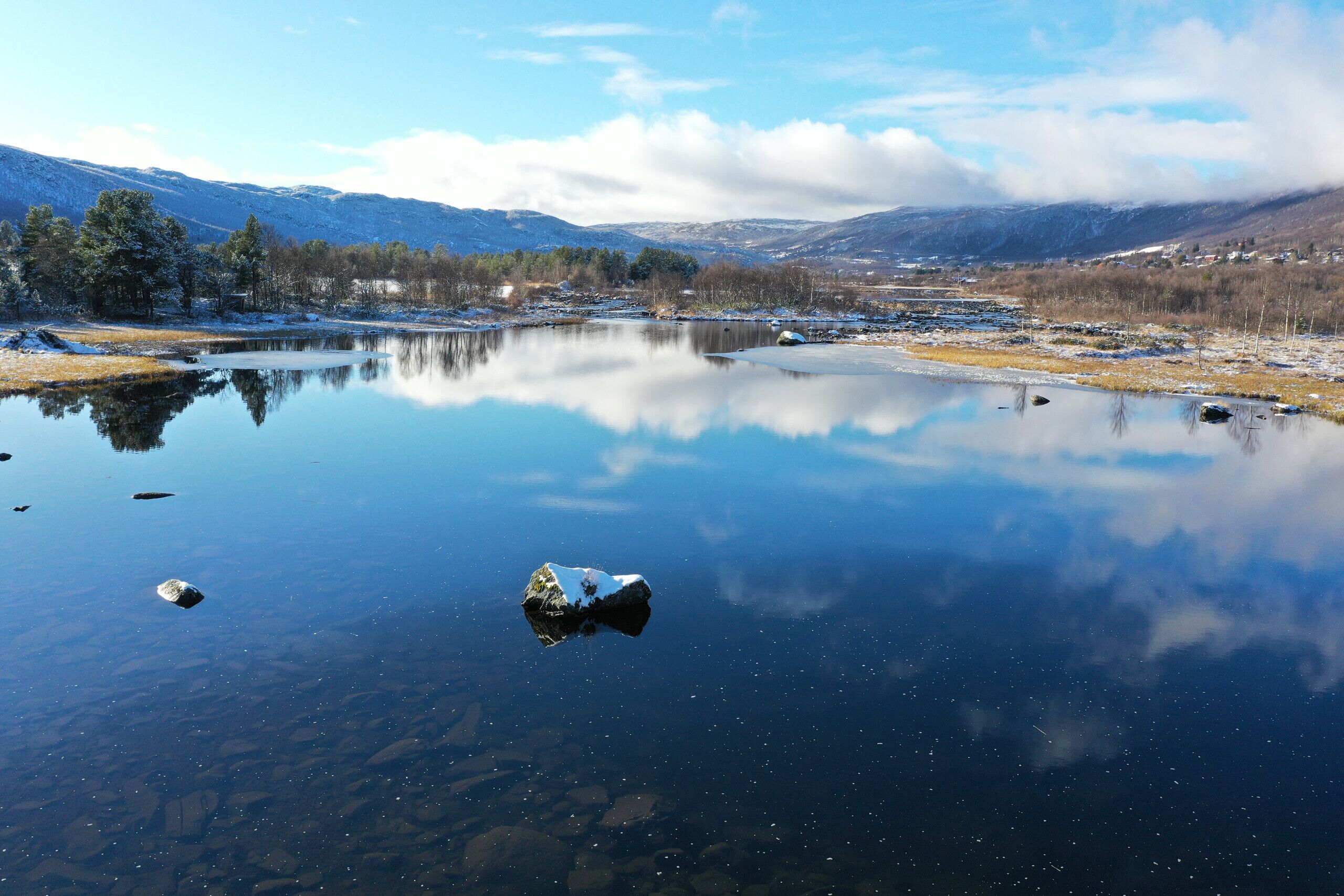 Een kalm meer met heldere reflecties, omgeven door bergen en enkele bomen.