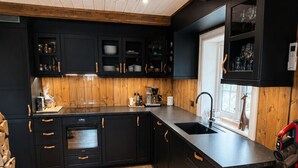 A modern kitchen with black cabinetry, wooden beams, a built-in wine rack, and a large window.