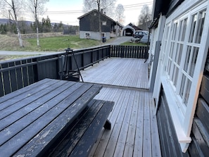 Une terrasse en bois avec un banc, un espace abrité et un garage contenant des véhicules.
