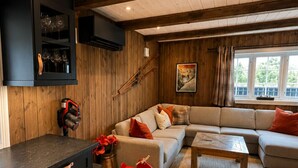 A cozy living room with a wooden ceiling, a sofa set, a coffee table, and a kitchen area with cabinets and a countertop.