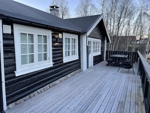 Une cabane en rondins avec une terrasse et deux fenêtres.