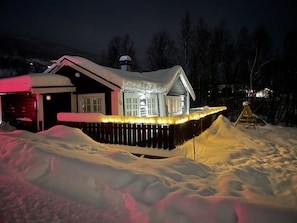 Une maison recouverte de neige, avec une terrasse en bois et un toit également enneigé.