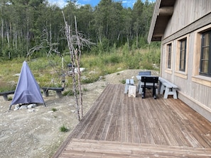 Une terrasse en bois avec une table et des bancs, entourée d’une forêt.