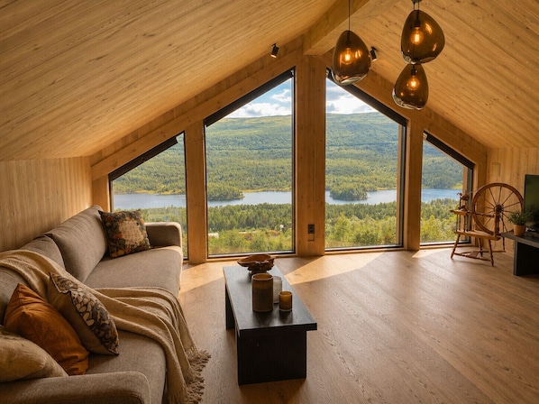 A cozy loft bedroom with a large window, wooden ceiling, and a spinning wheel.
