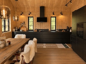 A modern kitchen with wooden walls, a black island, and pendant lighting.