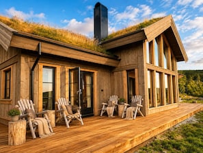 A wooden cabin with a deck, large windows, and a chimney.