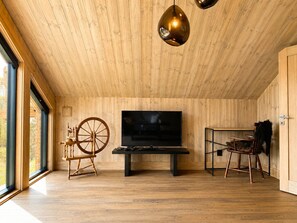 Ein Zimmer mit Holzwänden, einem großen Fernseher, einem Spinnrad und einem rustikalen Sessel.