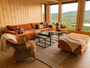 A cozy living room with a sofa, chairs, a coffee table, and a view of a forest and lake.