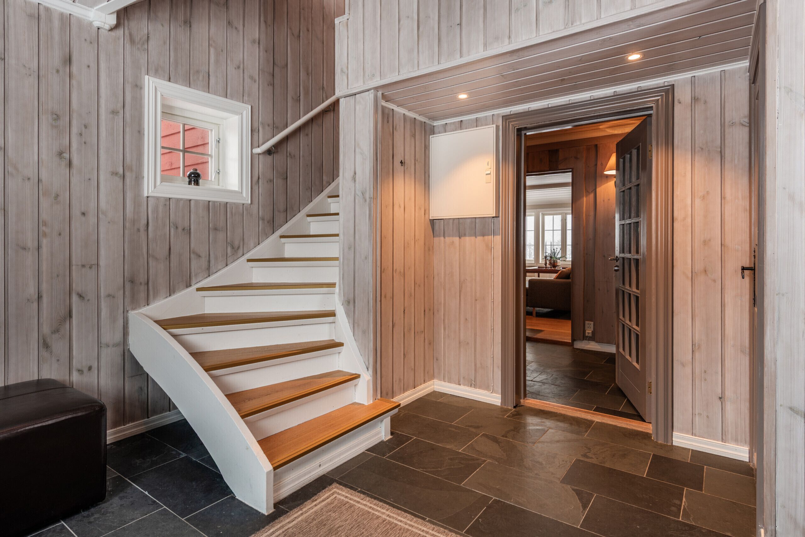 A wooden staircase leading to a second floor, a small window with a view, and a door to another room.