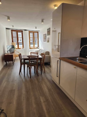 A modern kitchen with wooden cabinets, a dining area with a table and chairs, and a sofa.