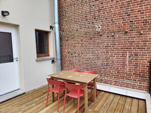 Una mesa de madera y sillas rojas frente a un edificio con un muro de ladrillo.