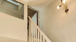 A bedroom with a bed, a staircase, a nightstand, and a wall-mounted light fixture.