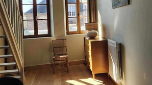 A room with a bed, a chair, a dresser, two windows, a radiator, and a staircase.