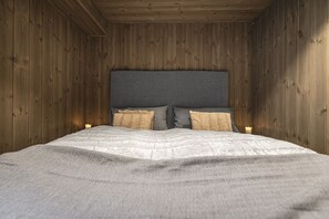 Ein Schlafzimmer mit einer Holzwand, einem grauen Kopfteil, zwei Kissen und einer weißen Bettdecke.