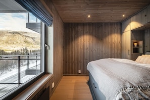 A bedroom with a large window, wooden walls, a bed, and a view of a snowy landscape. - Hemsedal ski in/ski out – new apartment with everything you need (Hemsedal)