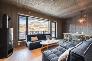 Ein gemütliches Zimmer mit großem Fenster, einer Couch, einem Esstisch und einem Kamin.