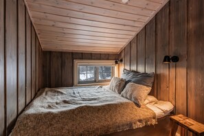 Ein Schlafzimmer mit Holzboden, einem Fenster, einem Bett mit Kissen und einem Nachttisch.