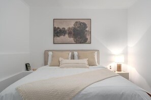 Ein Schlafzimmer mit einem Bett, einem Nachttisch, einer Lampe und einem gerahmten Bild an der Wand.