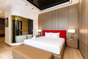 Camera d'albergo moderna con un letto grande, una testiera rossa, una cabina doccia in vetro e un pavimento in legno.
