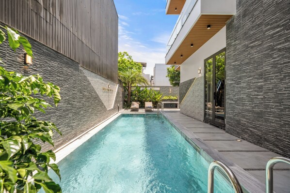 A modern outdoor swimming pool with a stone wall and a lounge area.
