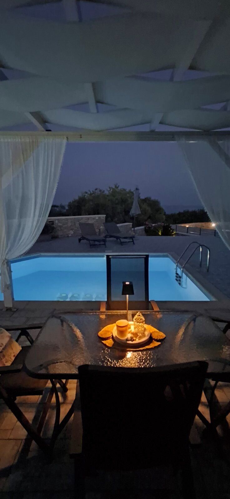 A poolside area with a table set for two, a chair, and a view of the pool.