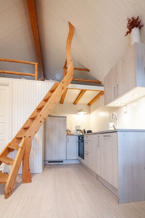 A modern kitchen with light wood cabinetry, a wooden staircase, and a built-in oven.
