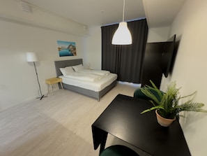 A modern hotel room with a bed, bedside table, lamp, potted plant, and a TV. - Studio Vestermyrveien, Svolvær (Vågan)