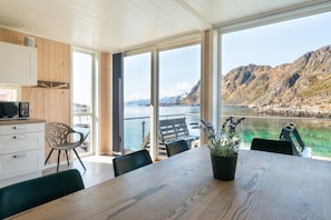 Uma cozinha moderna com armários de madeira, um espaço de refeições com mesa e cadeiras de madeira, e uma janela grande com vista para uma costa montanhosa.