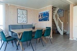 Ein Essbereich mit Holztisch, blaugrünen Stühlen, einem grauen Sofa und einer Treppe, die zu einer anderen Ebene führt.