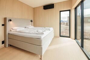 Un dormitori modern amb un llit gran, un panell de capçal integrat i una finestra gran amb vistes a l'exterior.