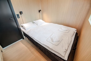 A neatly made bed with pillows and a folded towel, a bedside lamp, and a door with a handle.