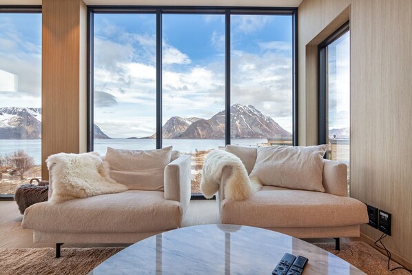 A modern living room with two sofas, a coffee table, and a large window offering a mountain view.
