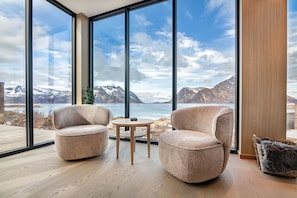 A modern room with large windows, two plush armchairs, a small wooden table, and a view of a mountainous landscape.