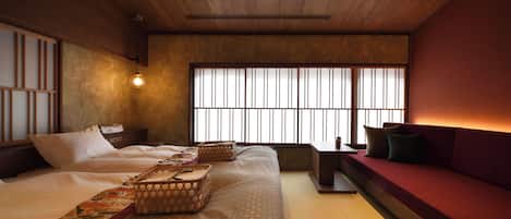 A traditional Japanese-style room with tatami flooring, a low wooden ceiling, a bed with a patterned bedspread, a red sofa, and a large window with vertical blinds.